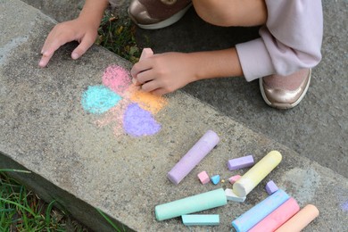 Photo of Little child drawing butterfly on curb outdoors, closeup