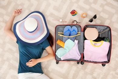 Photo of Young woman packing suitcase for summer journey at home, top view