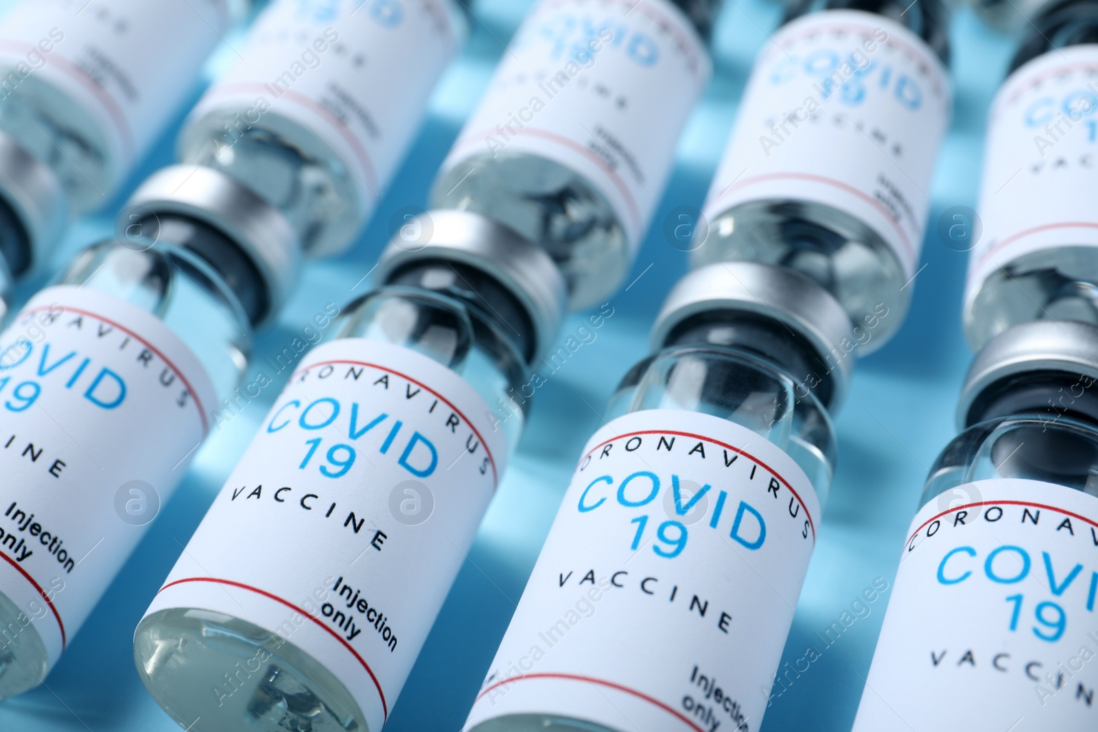 Photo of Glass vials with COVID-19 vaccine on light blue background