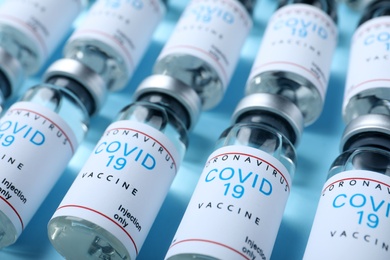 Glass vials with COVID-19 vaccine on light blue background