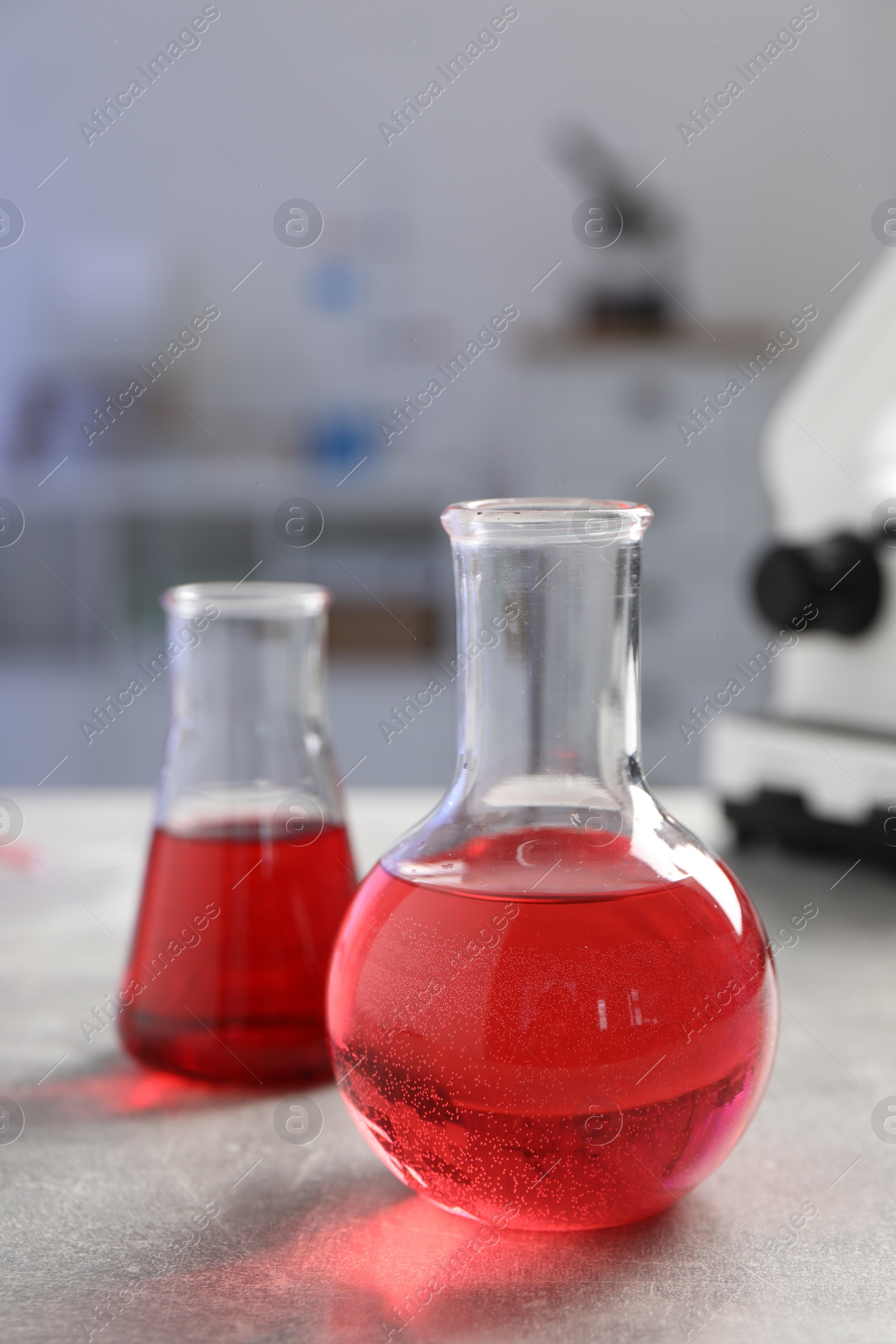 Photo of Laboratory analysis. Flasks with red liquid on light grey table, closeup