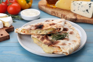 Photo of Tasty pizza calzones with cheese, rosemary and different products on light blue wooden table, closeup