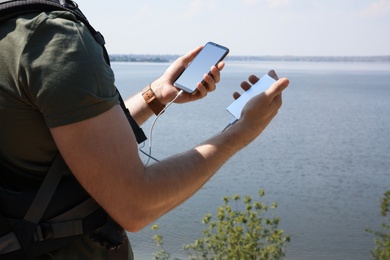 Man charging mobile phone with power bank near river, closeup