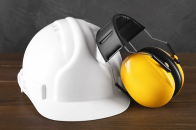 Photo of Hard hat and earmuffs on wooden table, closeup. Safety equipment