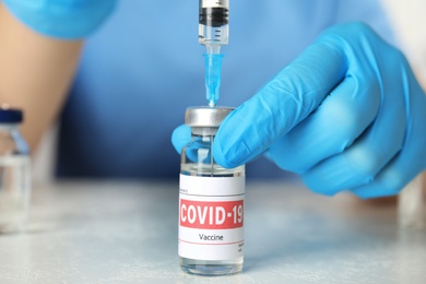 Doctor filling syringe with coronavirus vaccine at table in laboratory, closeup