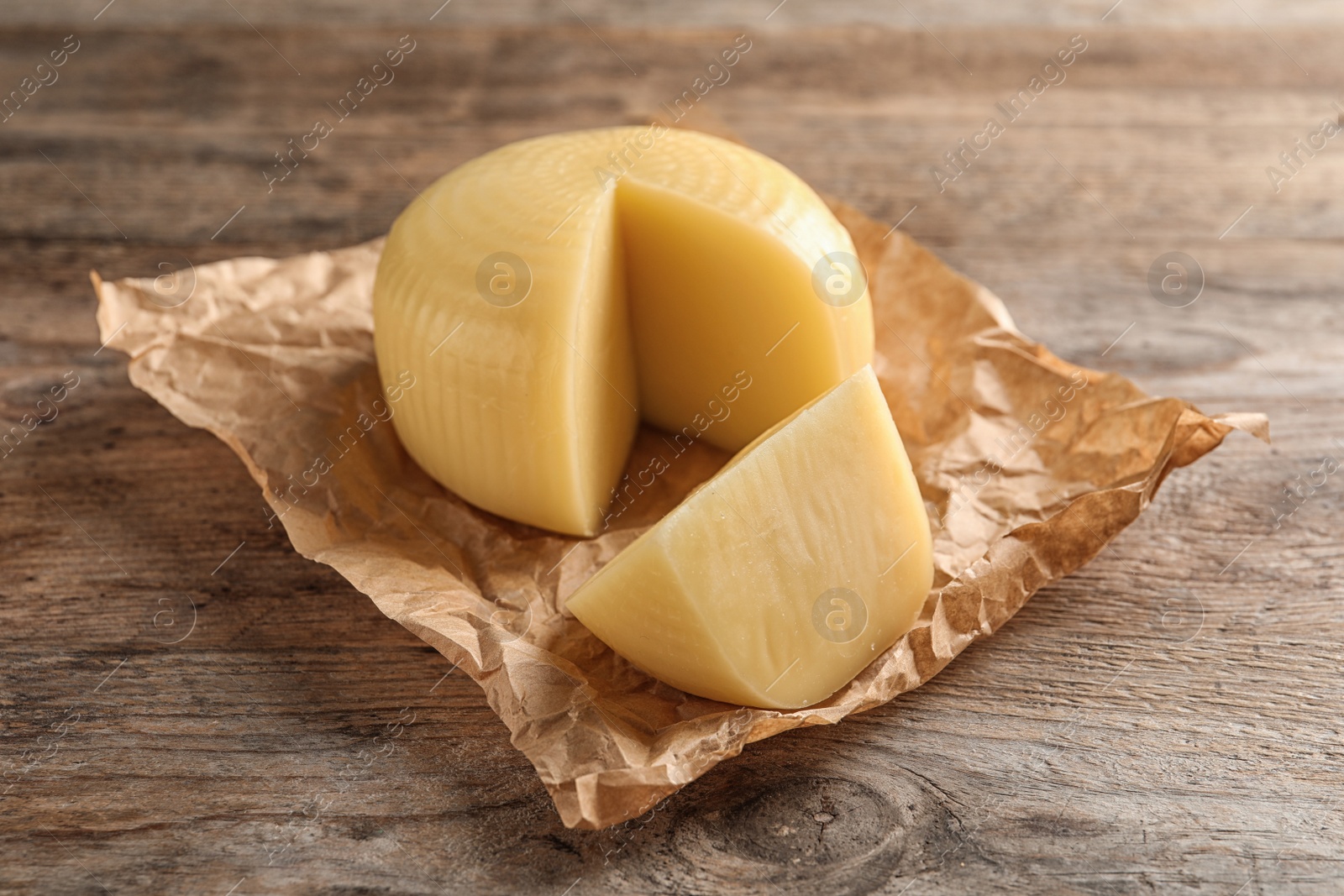 Photo of Parchment paper with cut wheel of delicious cheese on wooden table