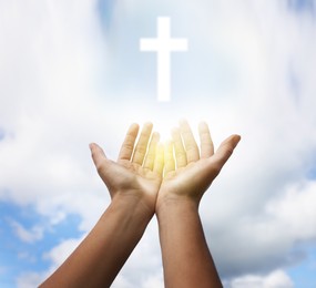 Woman stretching hands towards cross silhouette on blue sky, closeup. Praying concept