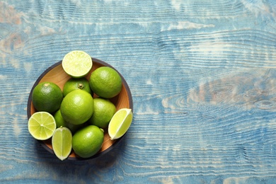 Photo of Bowl with fresh ripe limes on wooden background, top view