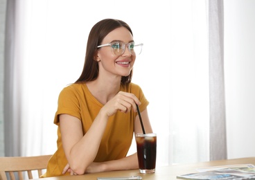 Young woman with glass of cola at table indoors. Refreshing drink