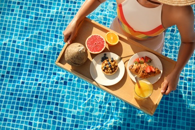 Photo of Young woman with delicious breakfast on tray in swimming pool, top view