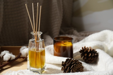 Reed air freshener, candle and pine cones on wooden tray indoors