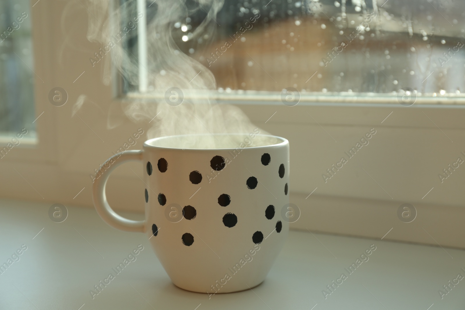 Photo of Cup of hot drink near window on rainy day