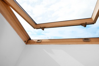 Photo of Beautiful view of cloudscape from open skylight roof window on slanted ceiling. Attic room