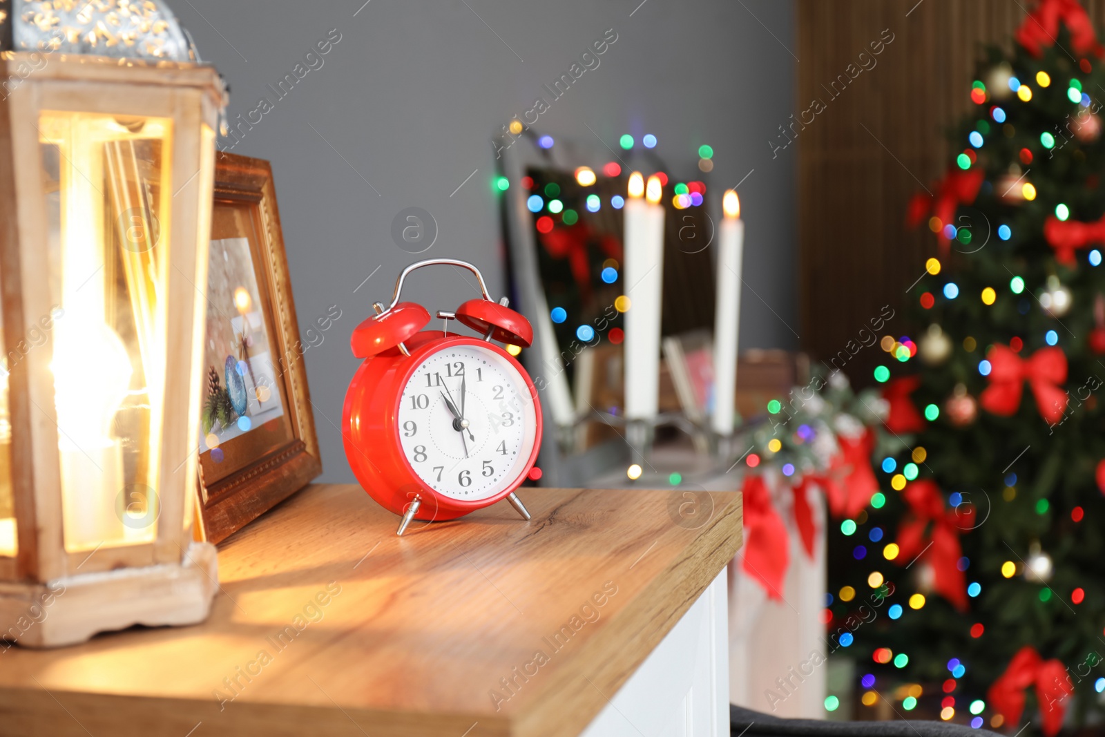 Photo of Alarm clock with lantern on chest of drawers and decorated Christmas tree in stylish living room interior