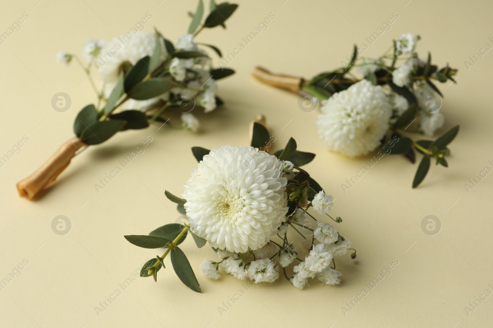 Photo of Many stylish boutonnieres on beige background, closeup