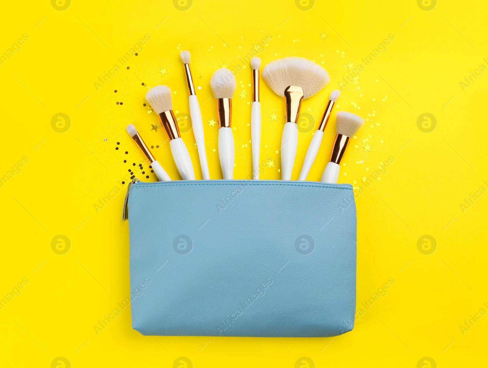 Photo of Different makeup brushes, case and shiny confetti on yellow background, flat lay