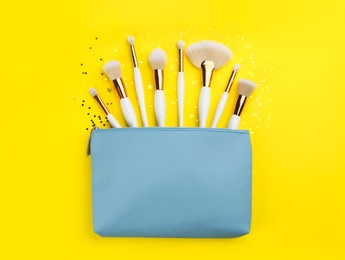 Photo of Different makeup brushes, case and shiny confetti on yellow background, flat lay