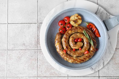 Delicious homemade sausage with garlic, tomatoes, rosemary and chili in frying pan on light tiled table, top view. Space for text