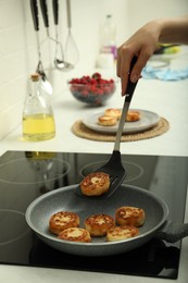 Photo of Woman frying delicious cottage cheese pancakes in kitchen, closeup