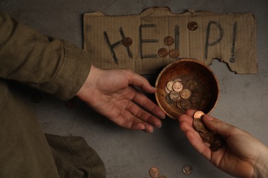 Photo of Woman giving coins to homeless, top view. Help sign and bowl with donations on cement