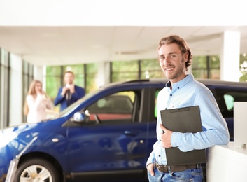 Salesman with clipboard near new car in modern auto dealership