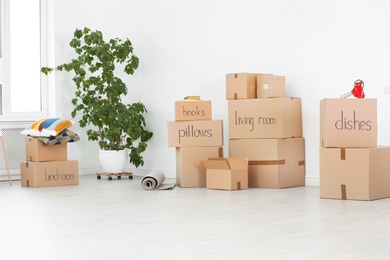 Photo of Cardboard boxes and household stuff near white wall indoors. Moving day