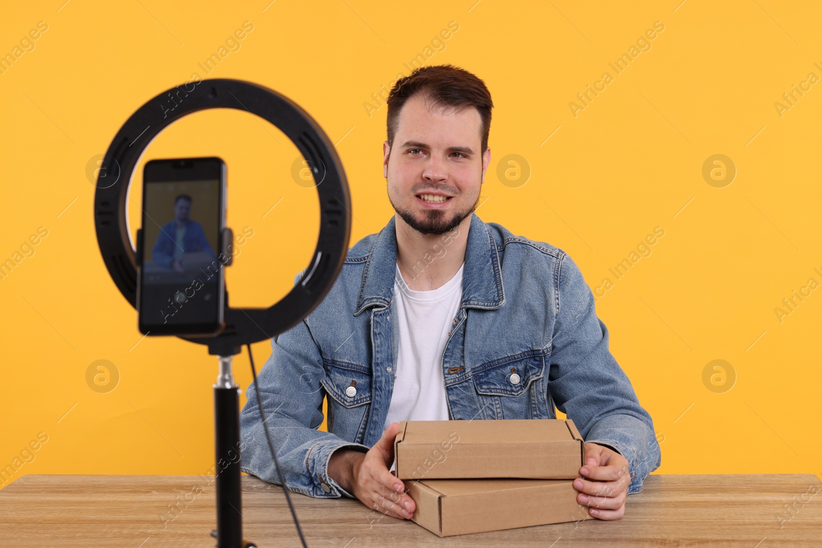 Photo of Smiling fashion blogger with parcels recording video at table against orange background