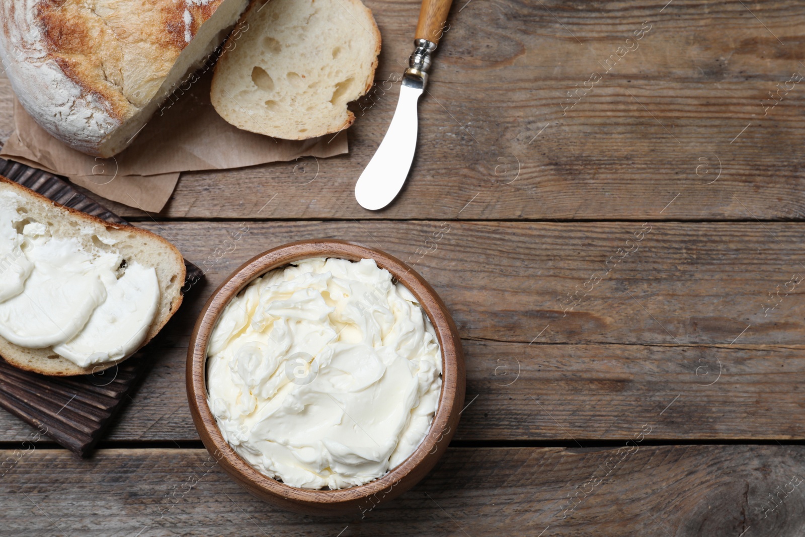 Photo of Fresh bread with delicious cream cheese on wooden table, flat lay. Space for text