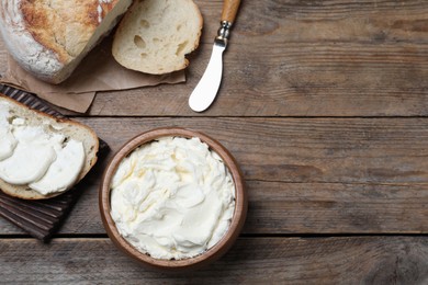 Photo of Fresh bread with delicious cream cheese on wooden table, flat lay. Space for text