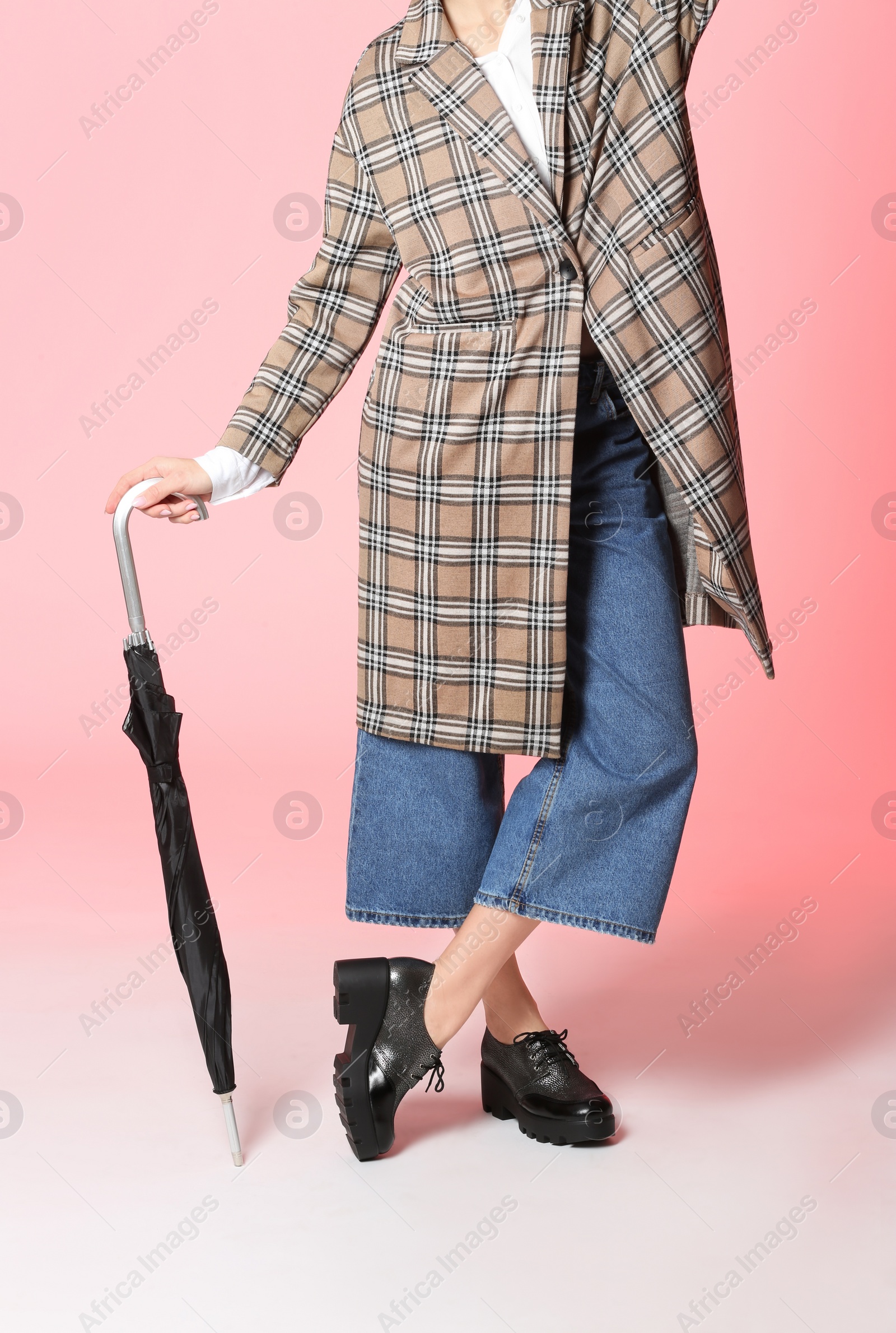 Photo of Woman in stylish shoes and coat holding umbrella on color background