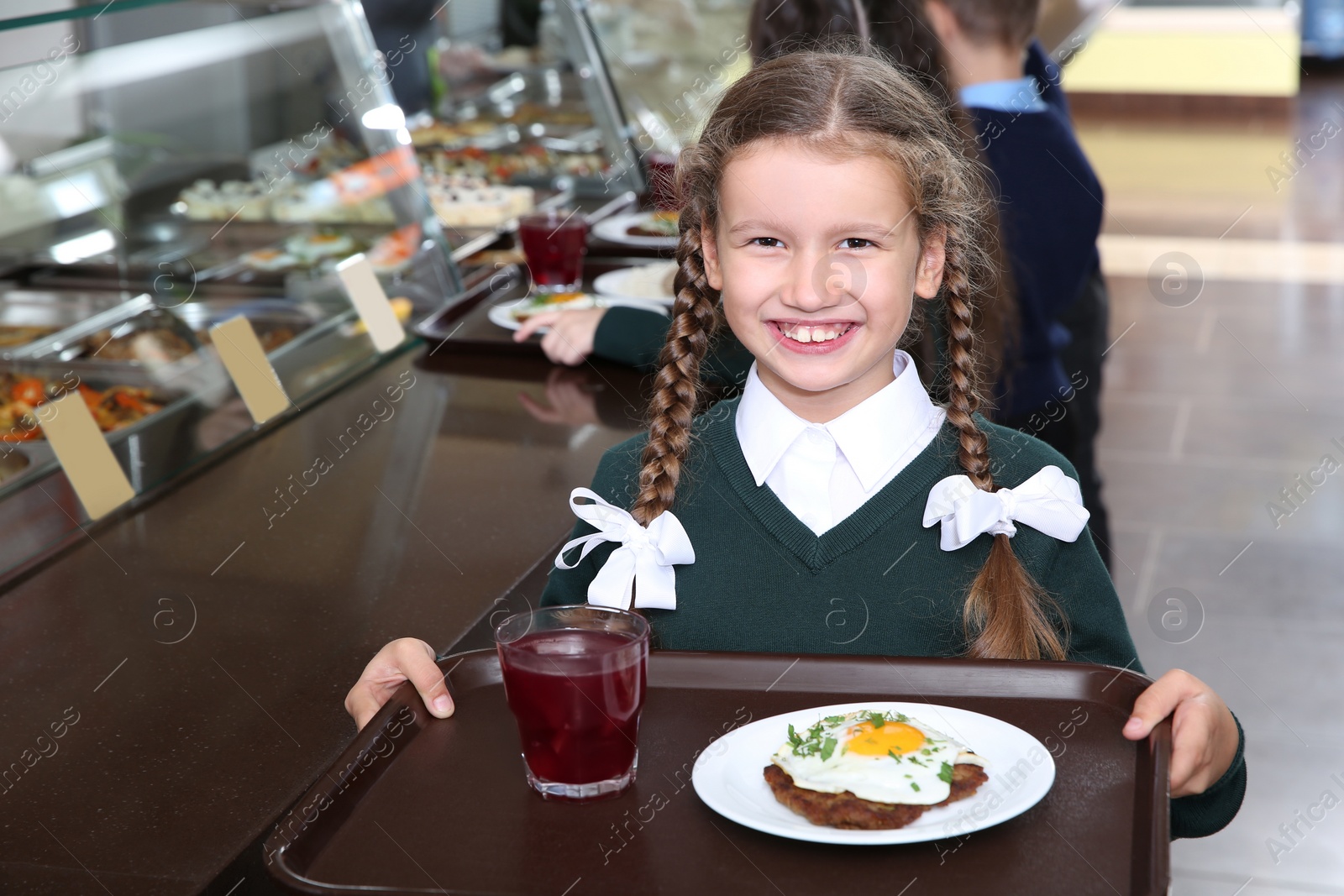 Photo of Cute girl holding tray with healthy food in school canteen