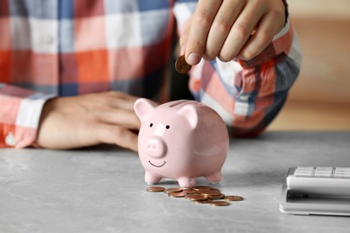 Man putting coin into piggy bank at grey marble table, closeup. Money savings