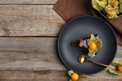 Piece of tasty cake decorated with physalis fruit on wooden table, flat lay. Space for text