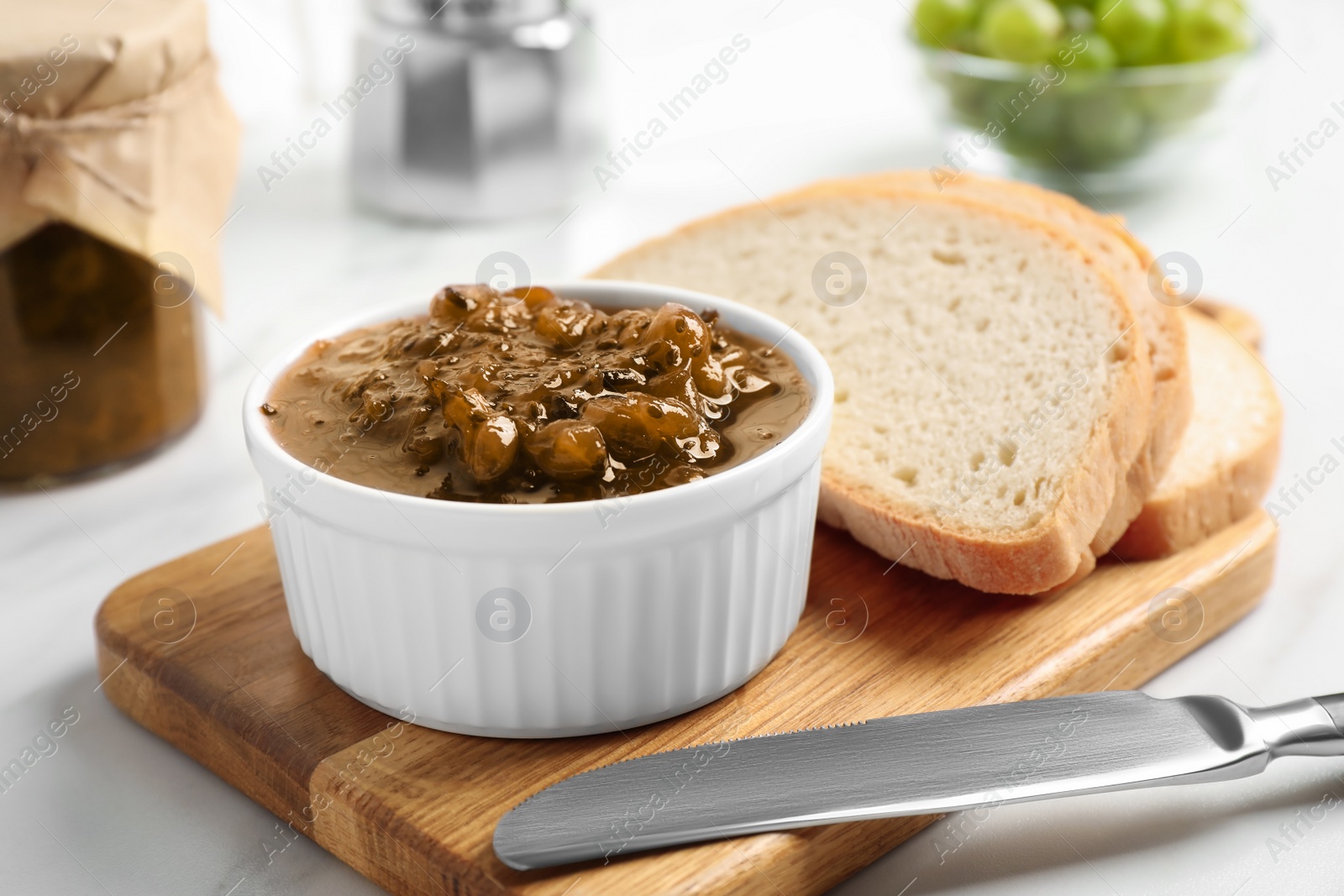 Photo of Delicious gooseberry jam and slices of bread on white table