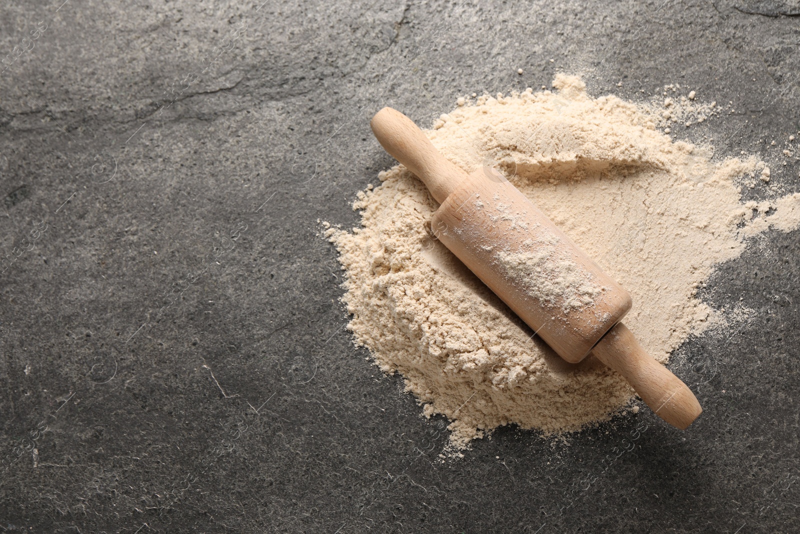 Photo of Scattered flour and rolling pin on grey textured table, above view. Space for text