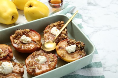 Photo of Tasty baked quinces with nuts and cream cheese in dish on white marble table, closeup. Space for text