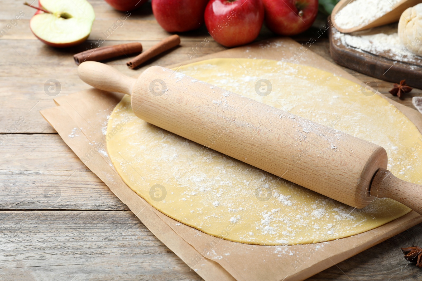 Photo of Rolling pin, raw dough and ingredients on wooden table, closeup. Baking apple pie