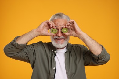 Photo of Senior man covering eyes with halves of kiwi on orange background