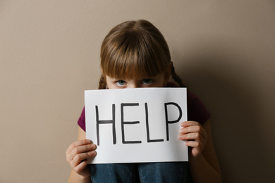 Photo of Sad little girl with sign HELP on beige background. Child in danger