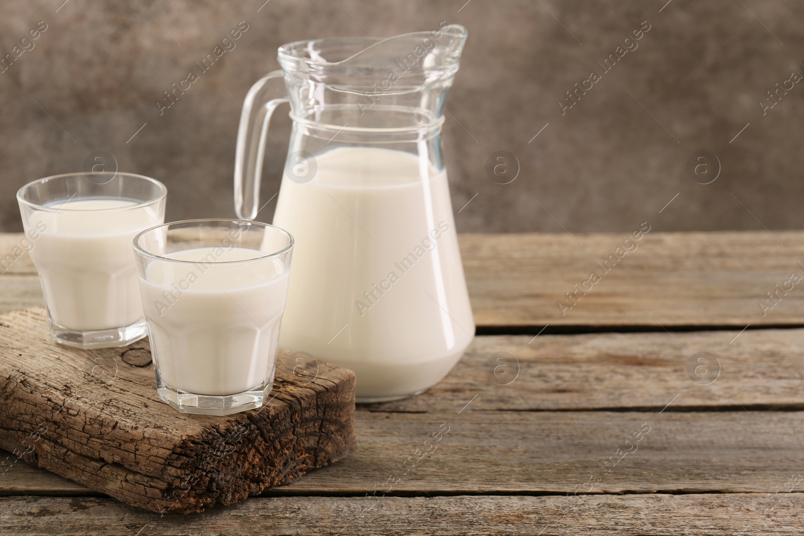 Photo of Jug and glasses of fresh milk on wooden table, space for text