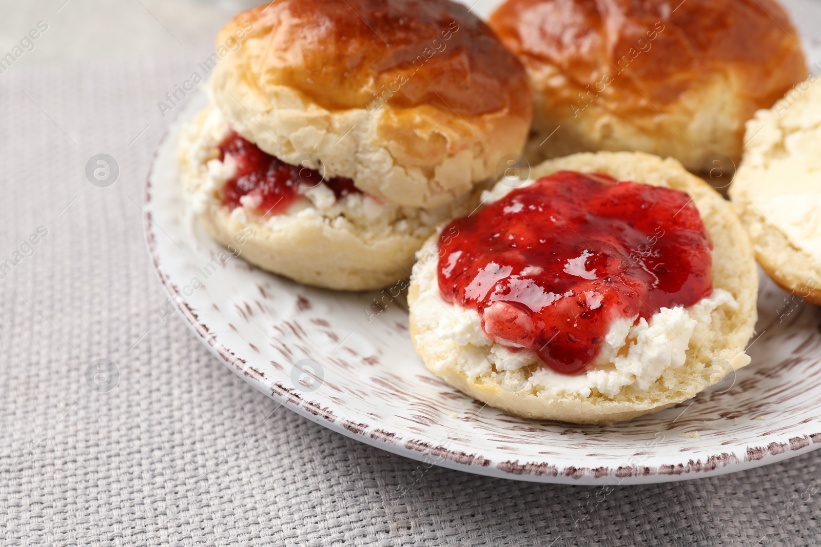 Photo of Freshly baked soda water scones with cranberry jam, butter and cup of tea on light grey mat, closeup