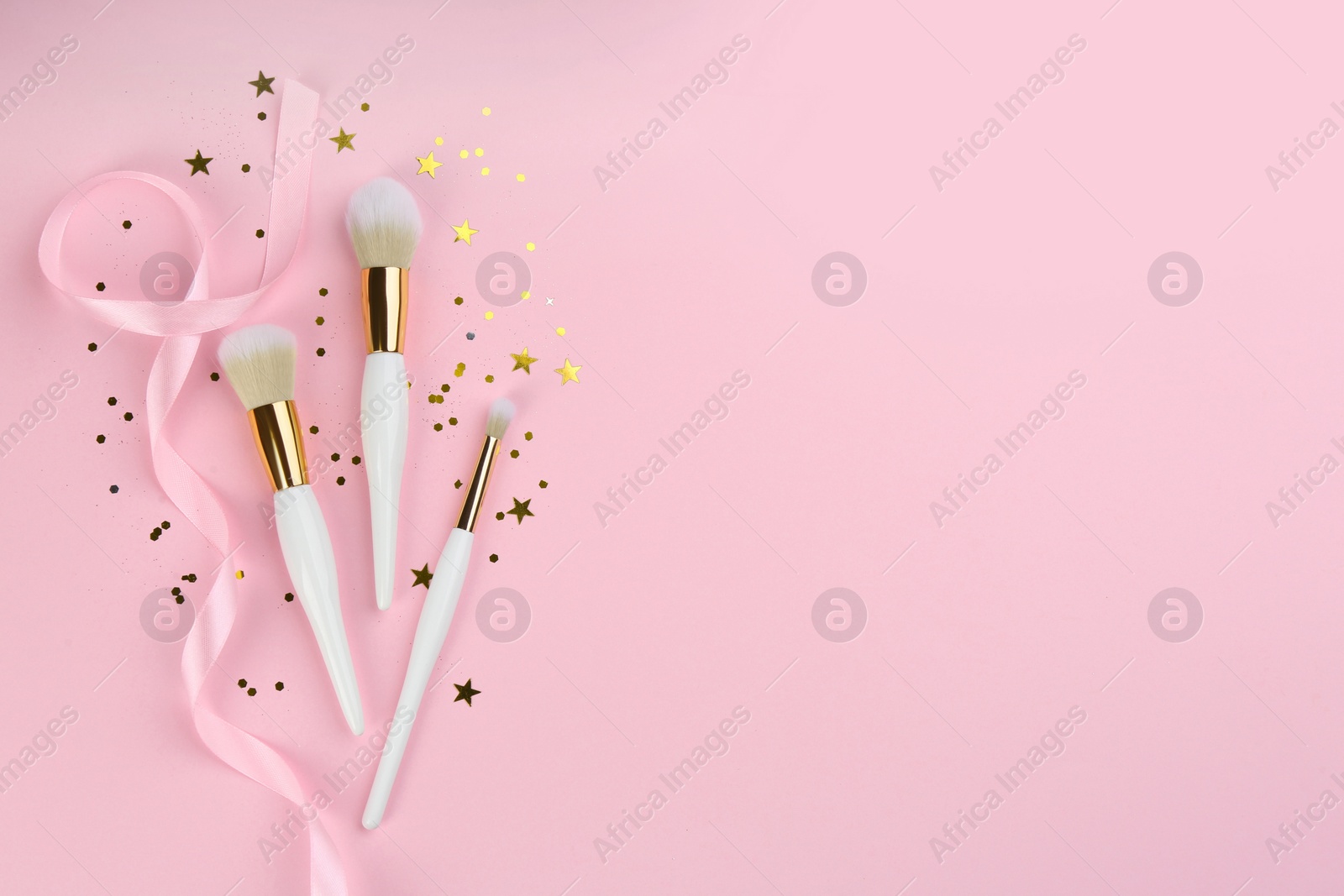 Photo of Different makeup brushes, ribbon and shiny confetti on pink background, flat lay. Space for text