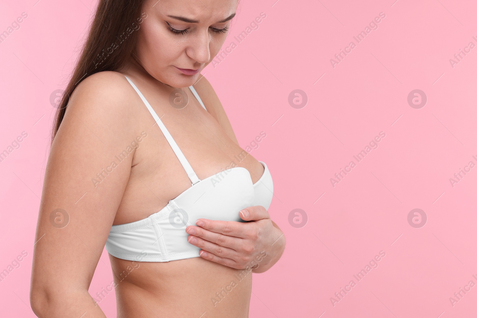 Photo of Mammology. Woman in bra doing breast self-examination on pink background, space for text