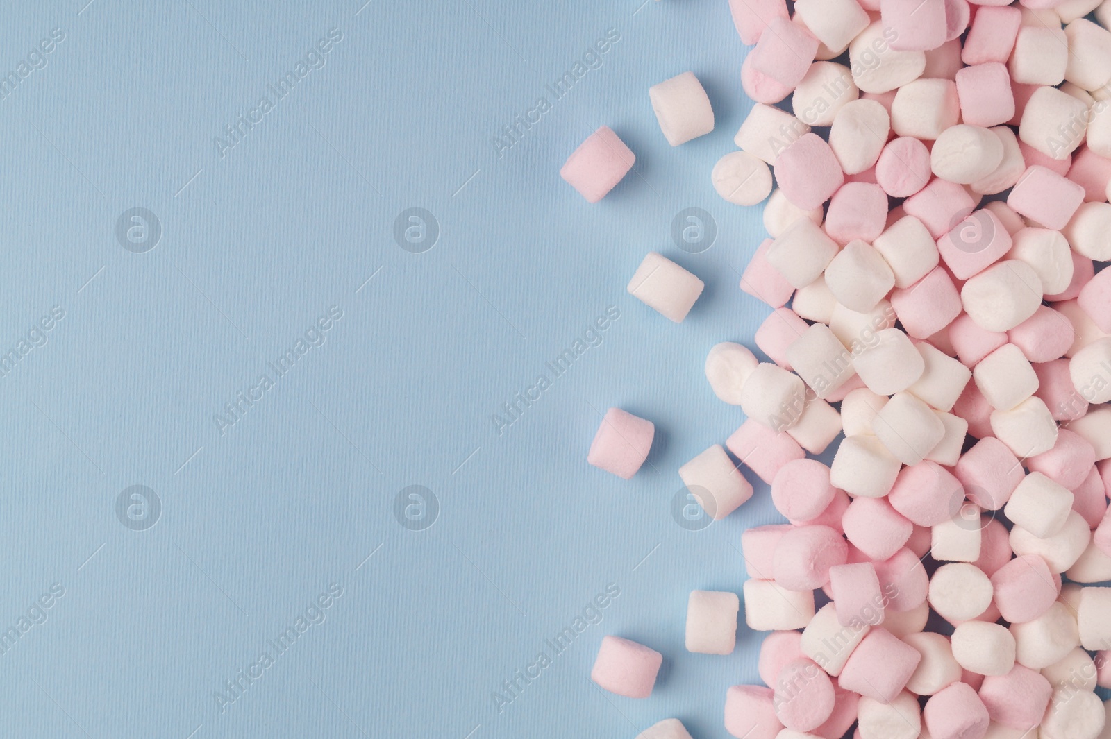 Photo of Delicious marshmallows on light blue background, flat lay. Space for text