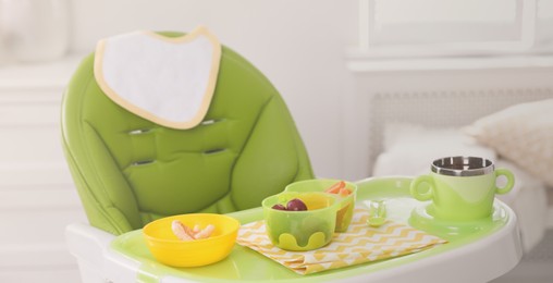 Image of High chair with food in baby tableware on tray indoors. Banner design