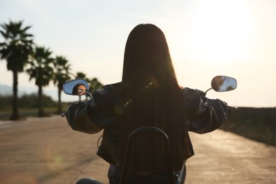 Photo of Woman riding motorcycle at sunset, back view