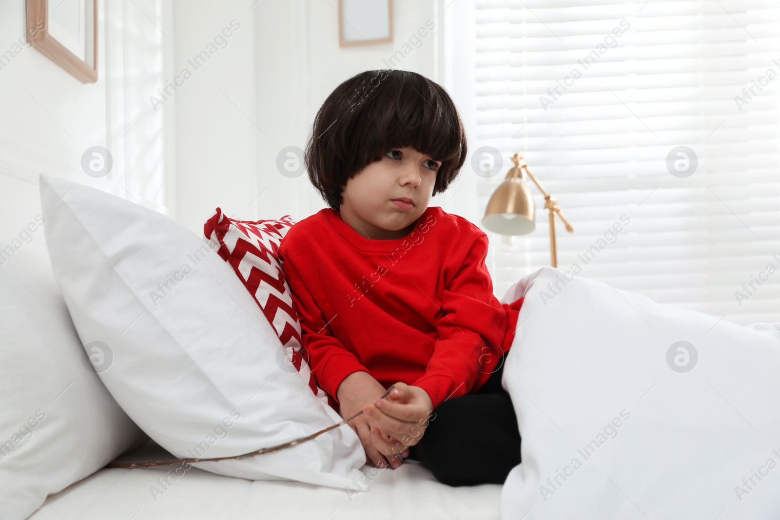 Photo of Sad little boy finding tree twig under pillow in bed at home. Saint Nicholas day tradition