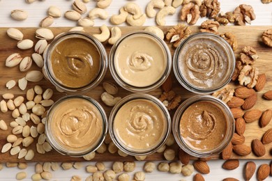 Many tasty nut butters in jars and nuts on white table, flat lay