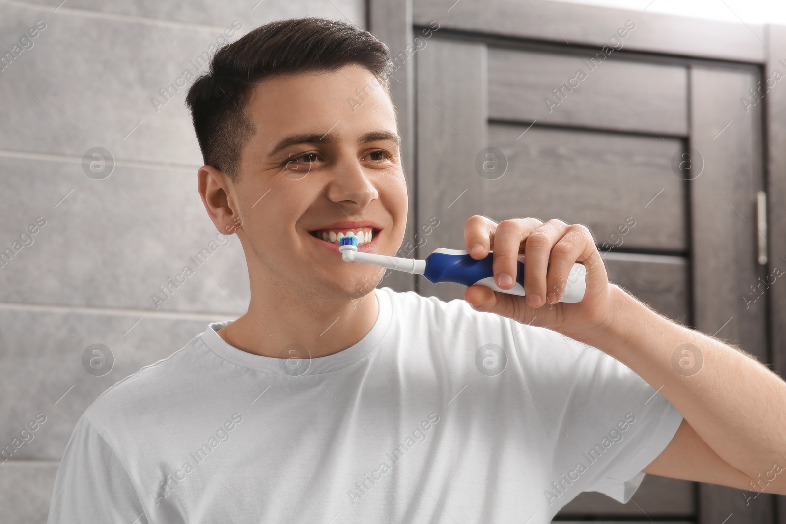 Photo of Man brushing his teeth with electric toothbrush in bathroom