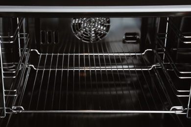 Photo of Open empty electric oven with rack, closeup. Inside view